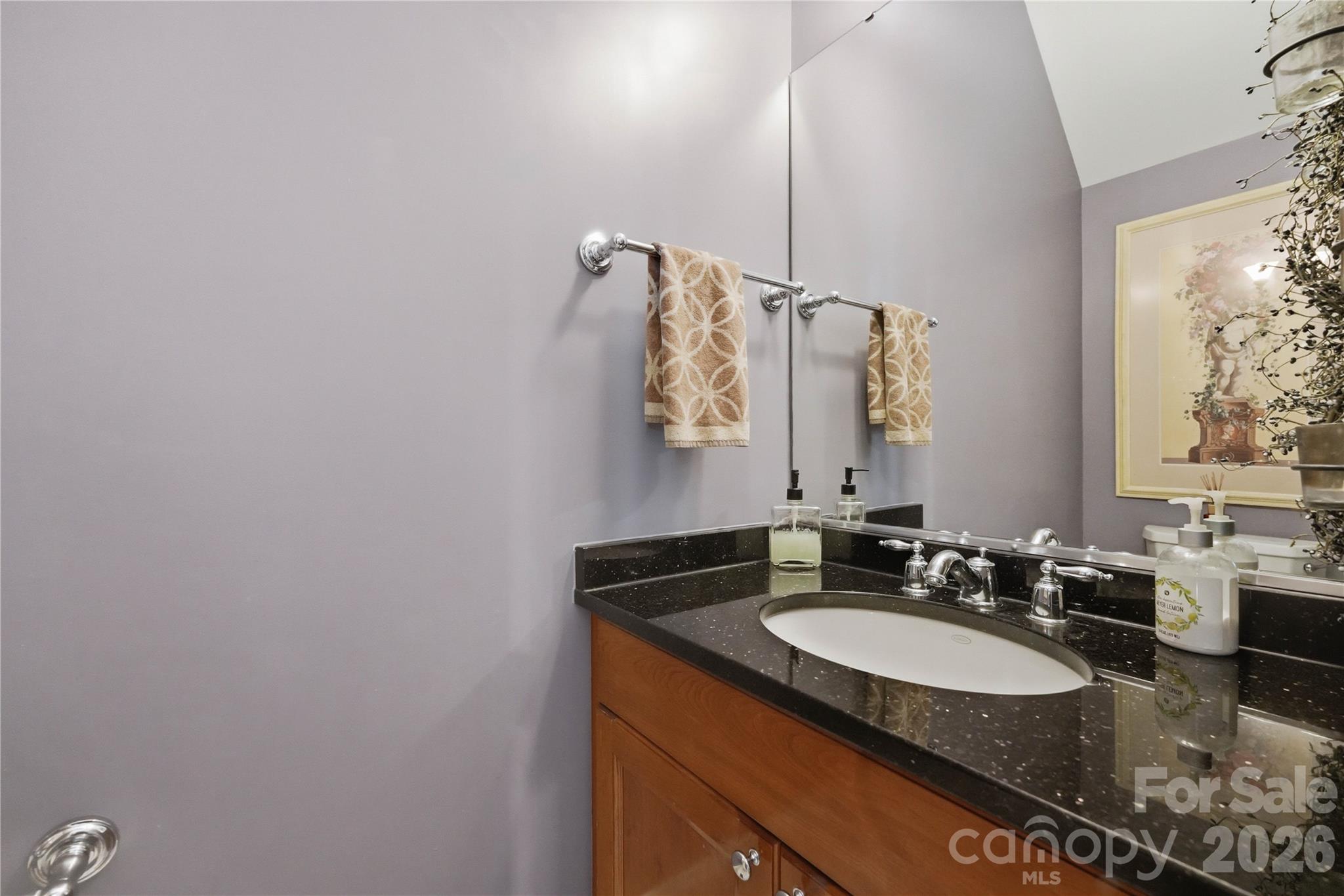 Bathroom vanity with a dark speckled counter, oval sink, chrome fixtures, and warm wood cabinetry.