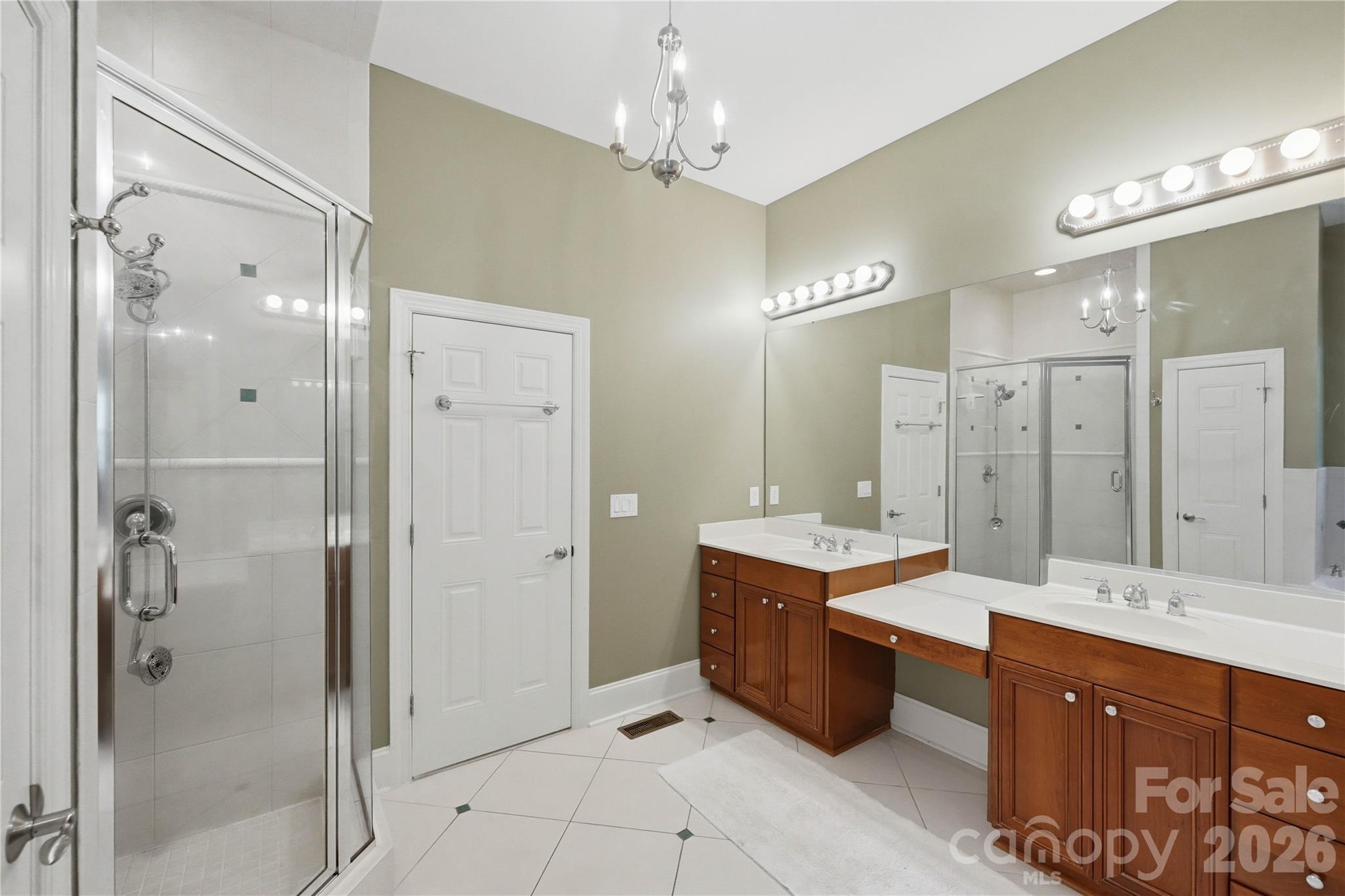 Bathroom with a glass shower, double wood vanities, large mirrors, and white tile flooring.