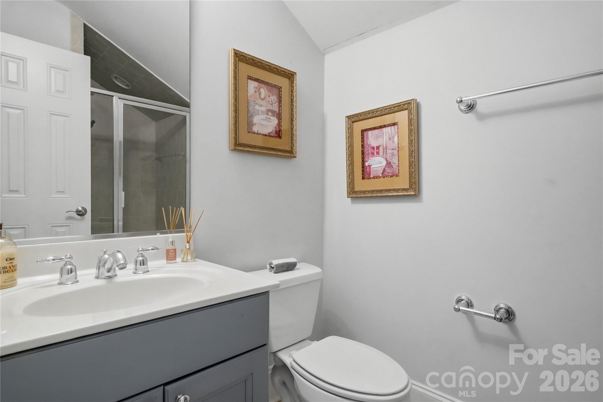 Bathroom with a gray vanity, glass shower, and toilet beneath two framed prints.