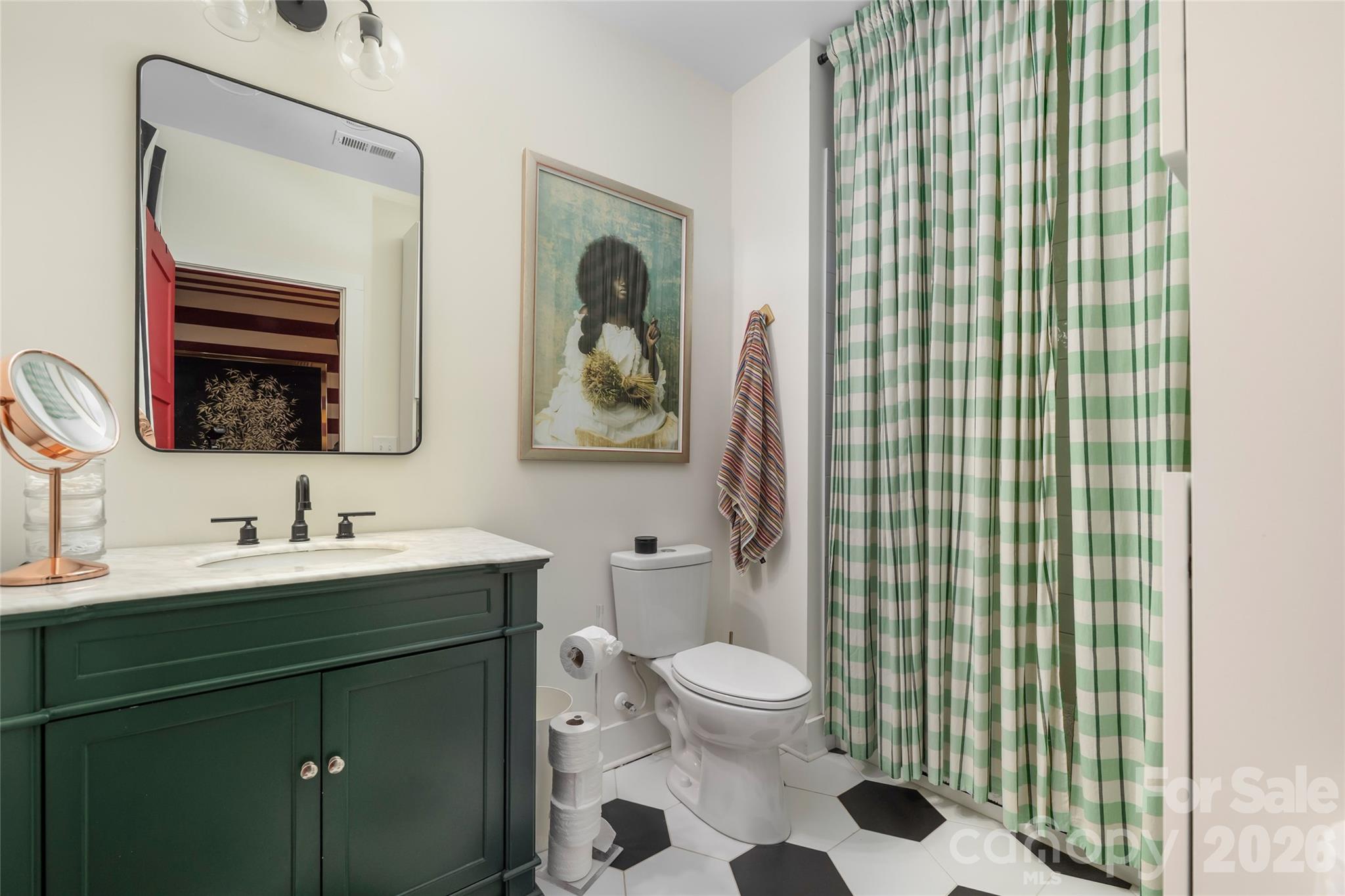 Bathroom with a dark green vanity, checked shower curtain, and black-and-white hexagonal floor tiles.