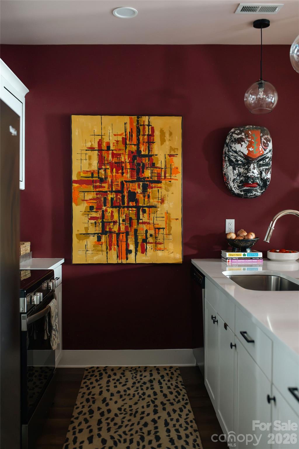 Kitchen with white cabinetry, burgundy walls, abstract artwork, and a patterned runner.