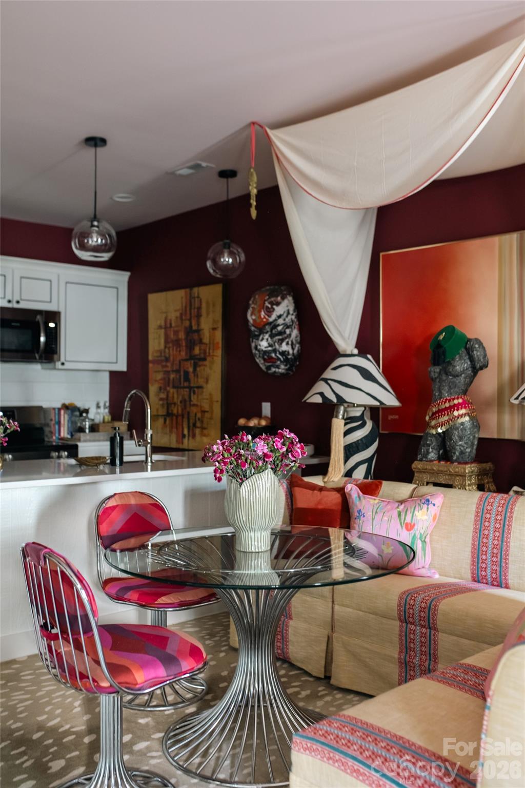 Dining area with a glass pedestal table, vivid pink chairs, and a cream banquette against burgundy walls.