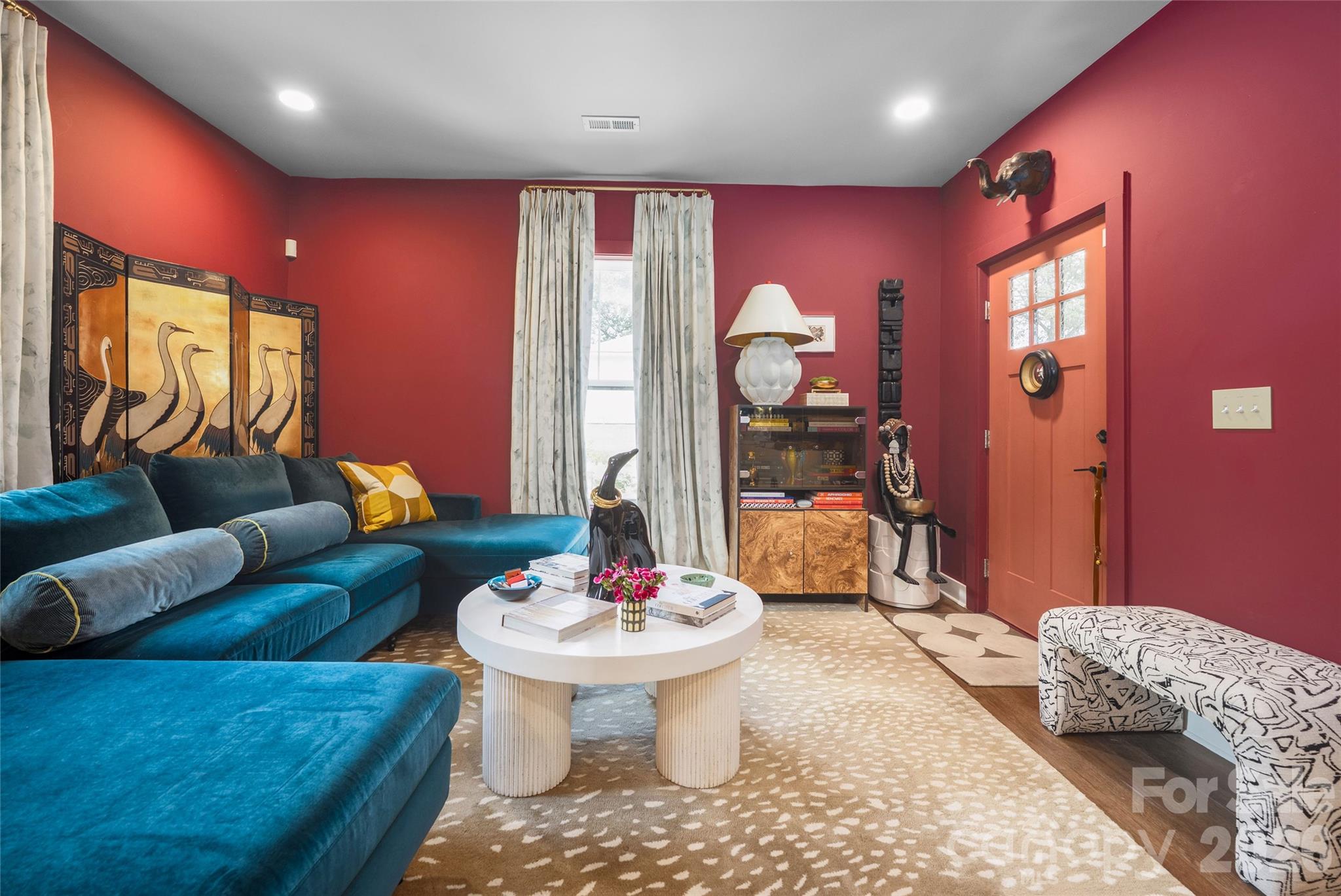 Red-walled living room with a teal sectional, white round coffee table, and orange-red entry door.