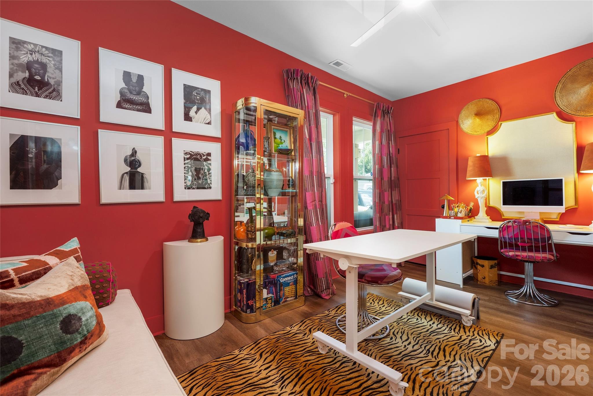 Furnished office with vivid red walls, framed portraits, a white desk, and tiger-striped rug.