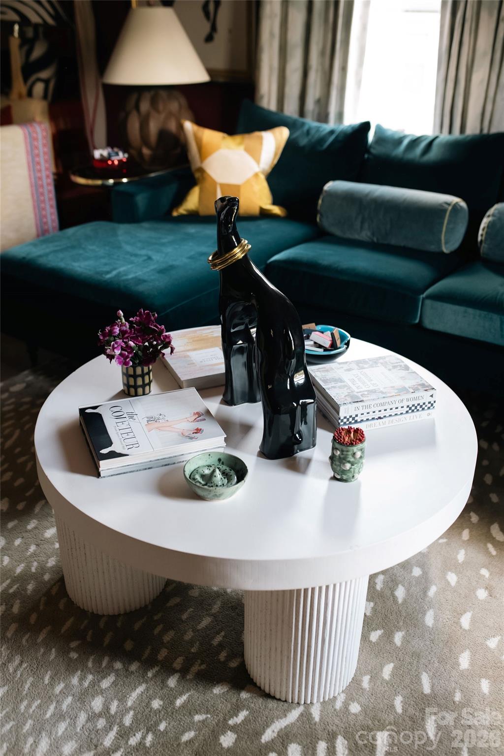 Living room with a teal sectional and a round white coffee table topped with books and sculptural decor.