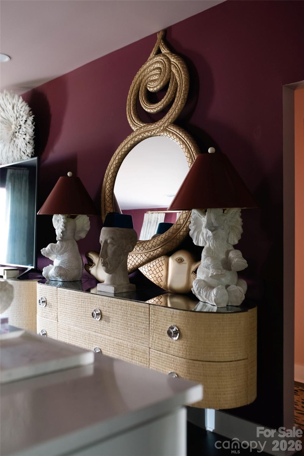 Burgundy accent wall with an ornate gold mirror above a console table and sculptural lamps.
