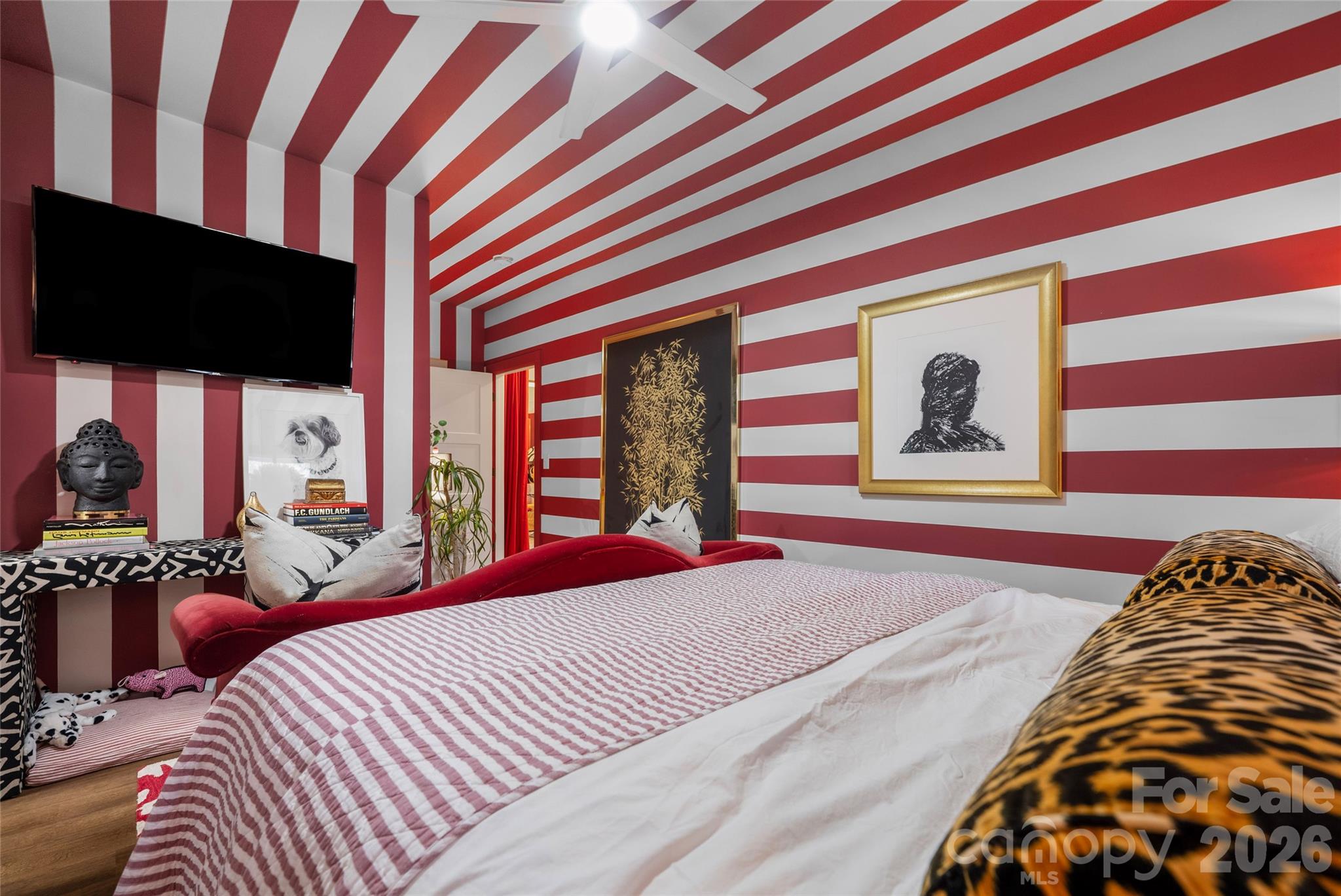 Bedroom with red-and-white striped walls and ceiling, striped bedding, leopard-print pillows, and wall-mounted television.