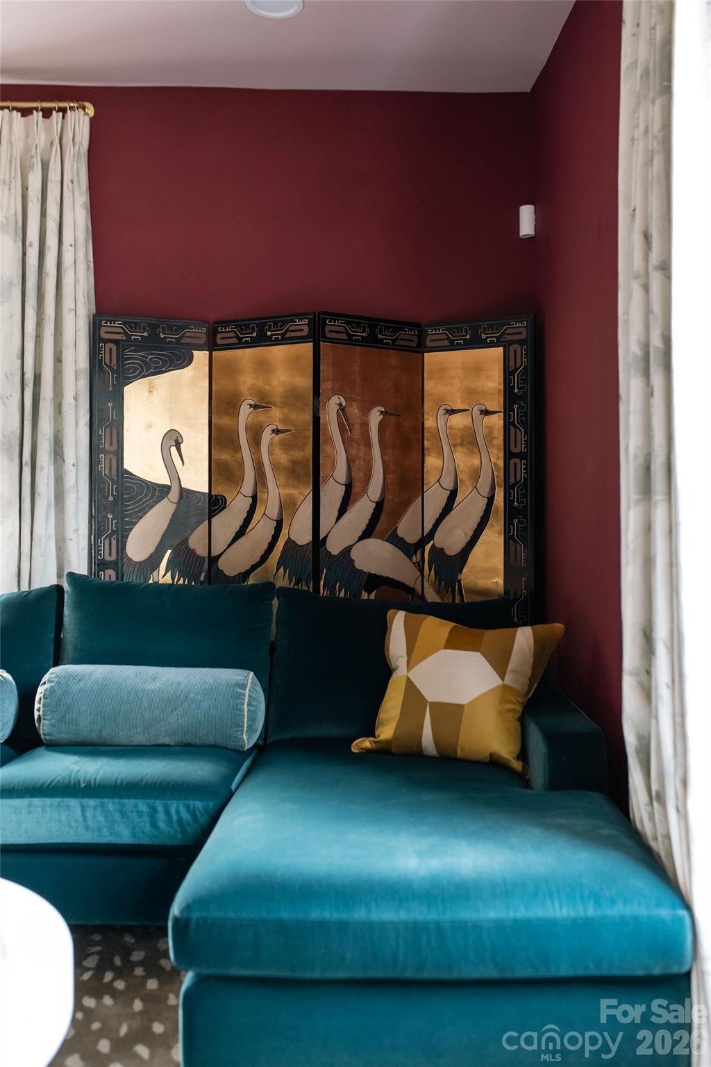 Living room with a teal sectional sofa and a decorative bird screen against burgundy walls.