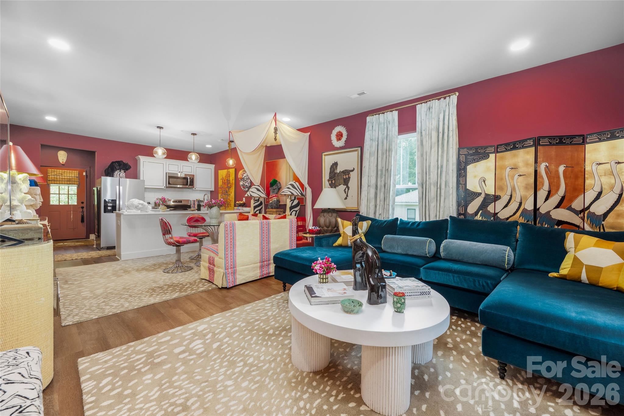 Living room with a teal sectional, burgundy walls, and an adjoining white kitchen.