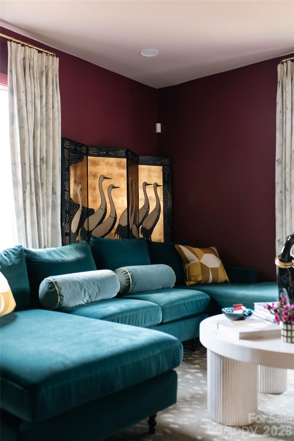 Living room with a teal sectional, burgundy walls, and a decorative crane screen.
