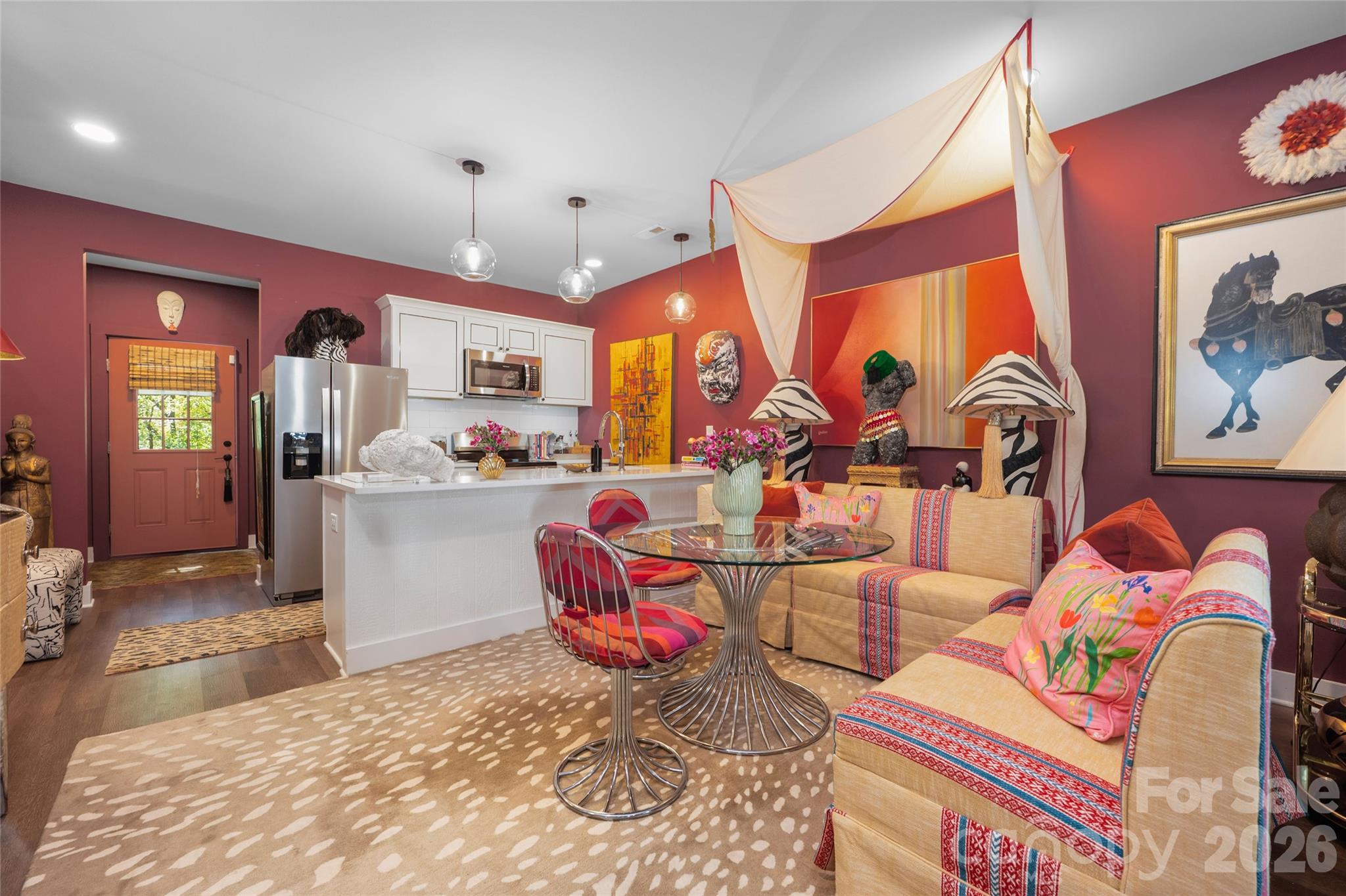 Open-plan living and kitchen area with burgundy walls, a white island, and vivid patterned furnishings.