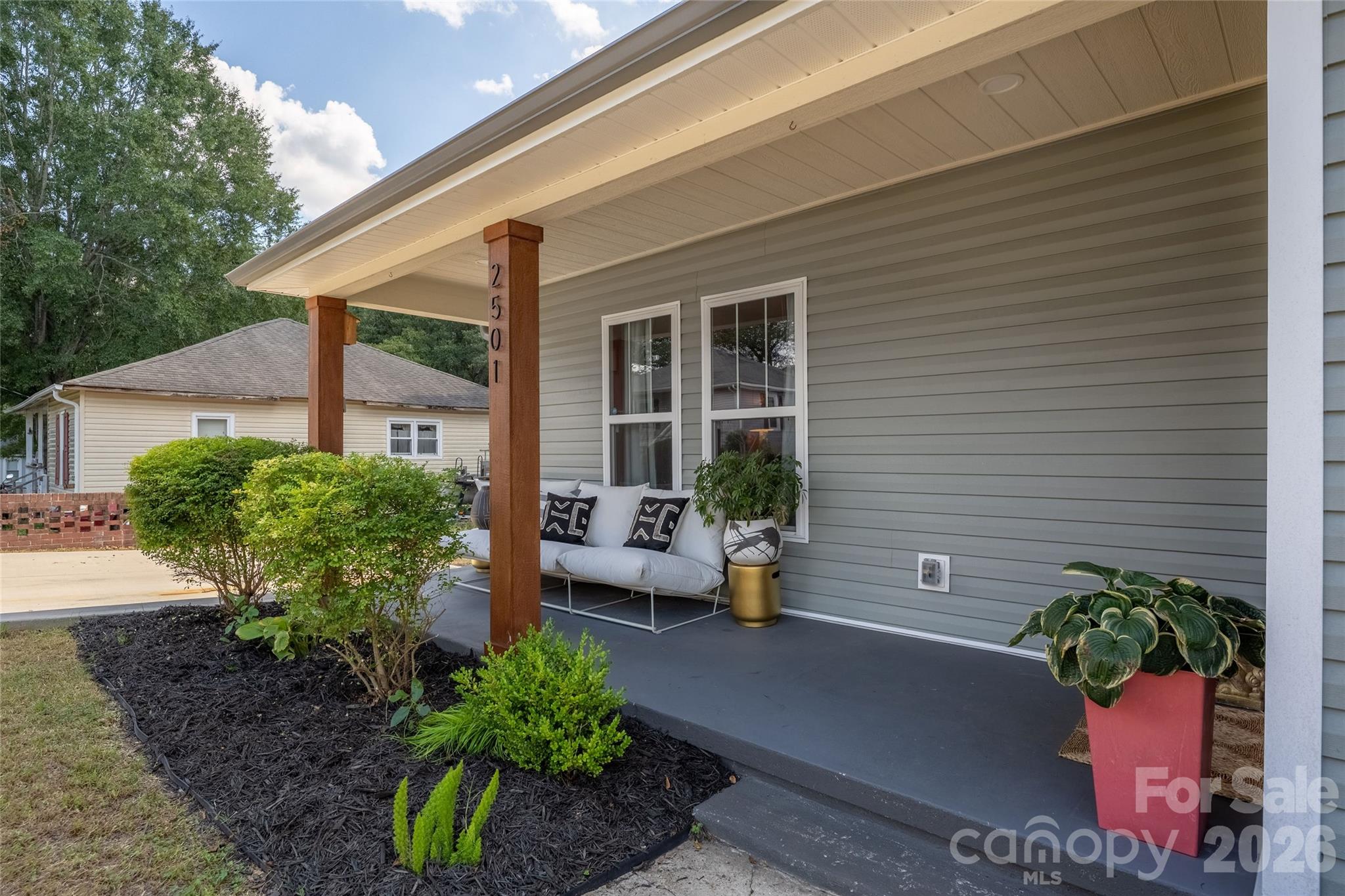Covered front porch with a white sofa, wooden posts, and landscaped shrubs.