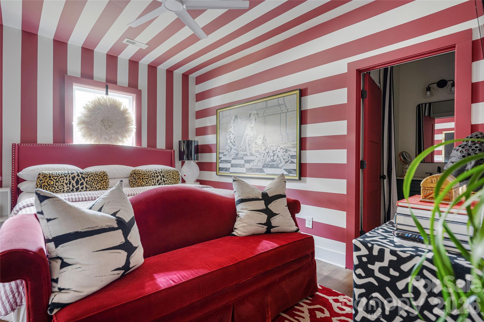 Bedroom with red-and-white striped walls, a red upholstered bed, patterned pillows, and framed artwork.
