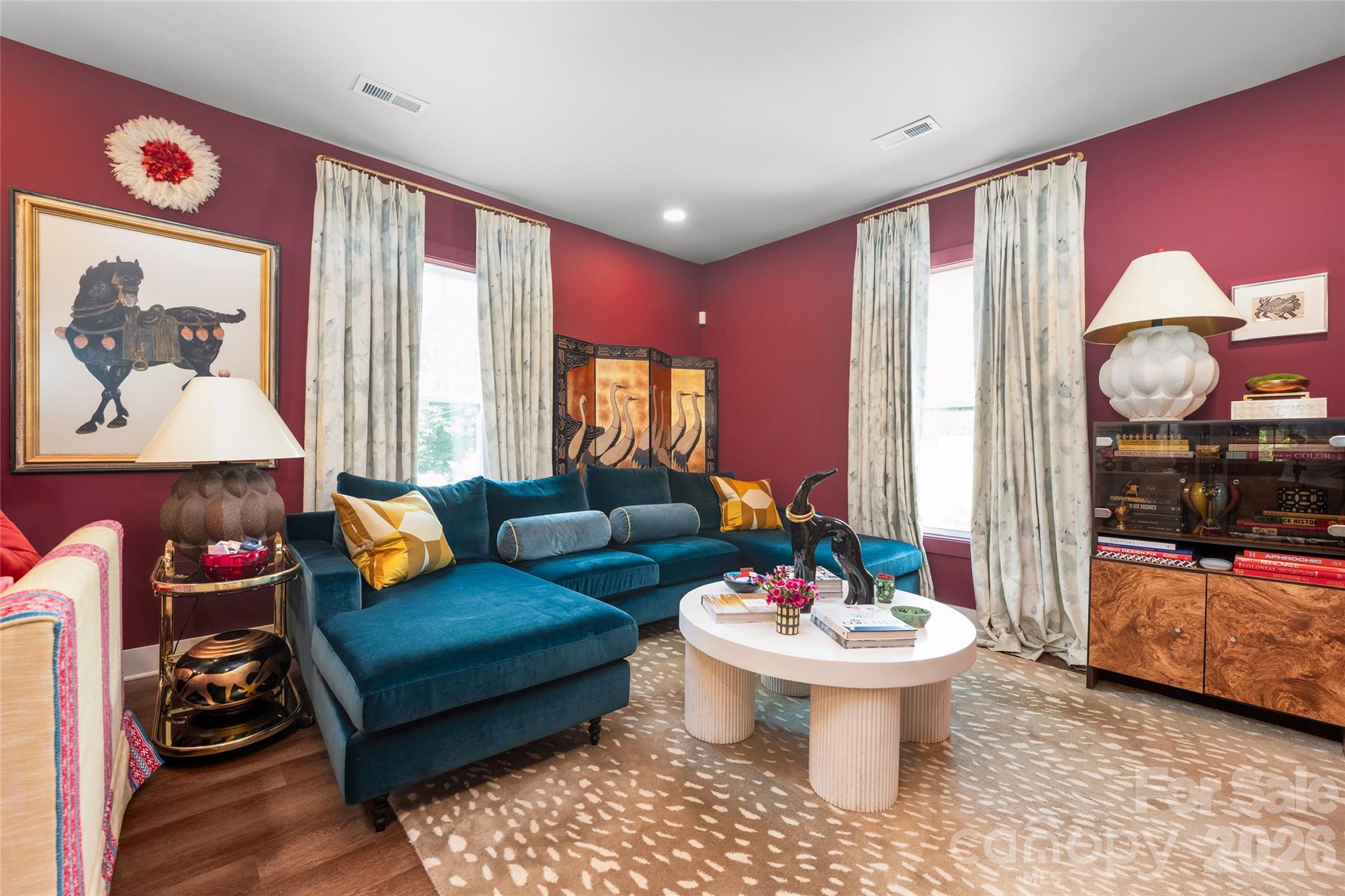 Burgundy living room with a teal sectional, patterned curtains, and a round white coffee table.