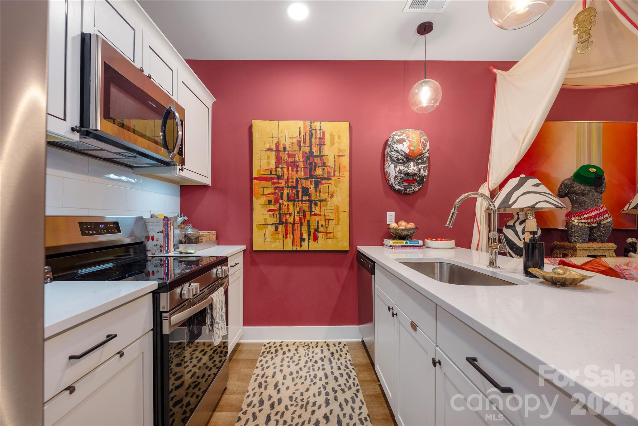Kitchen with white cabinetry, stainless steel appliances, and a red wall with bold artwork.