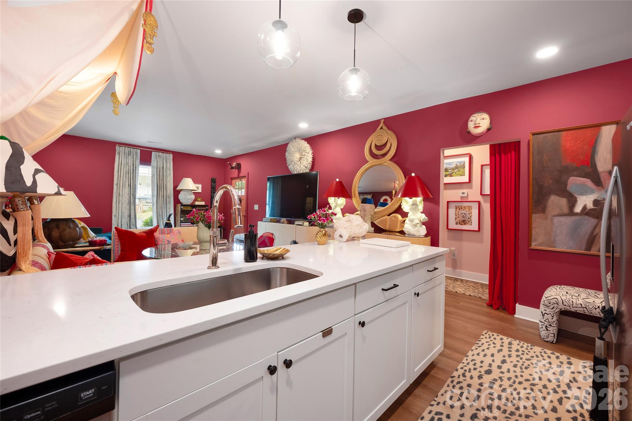 Kitchen with a large white island and sink opening onto a living area with vivid red walls.
