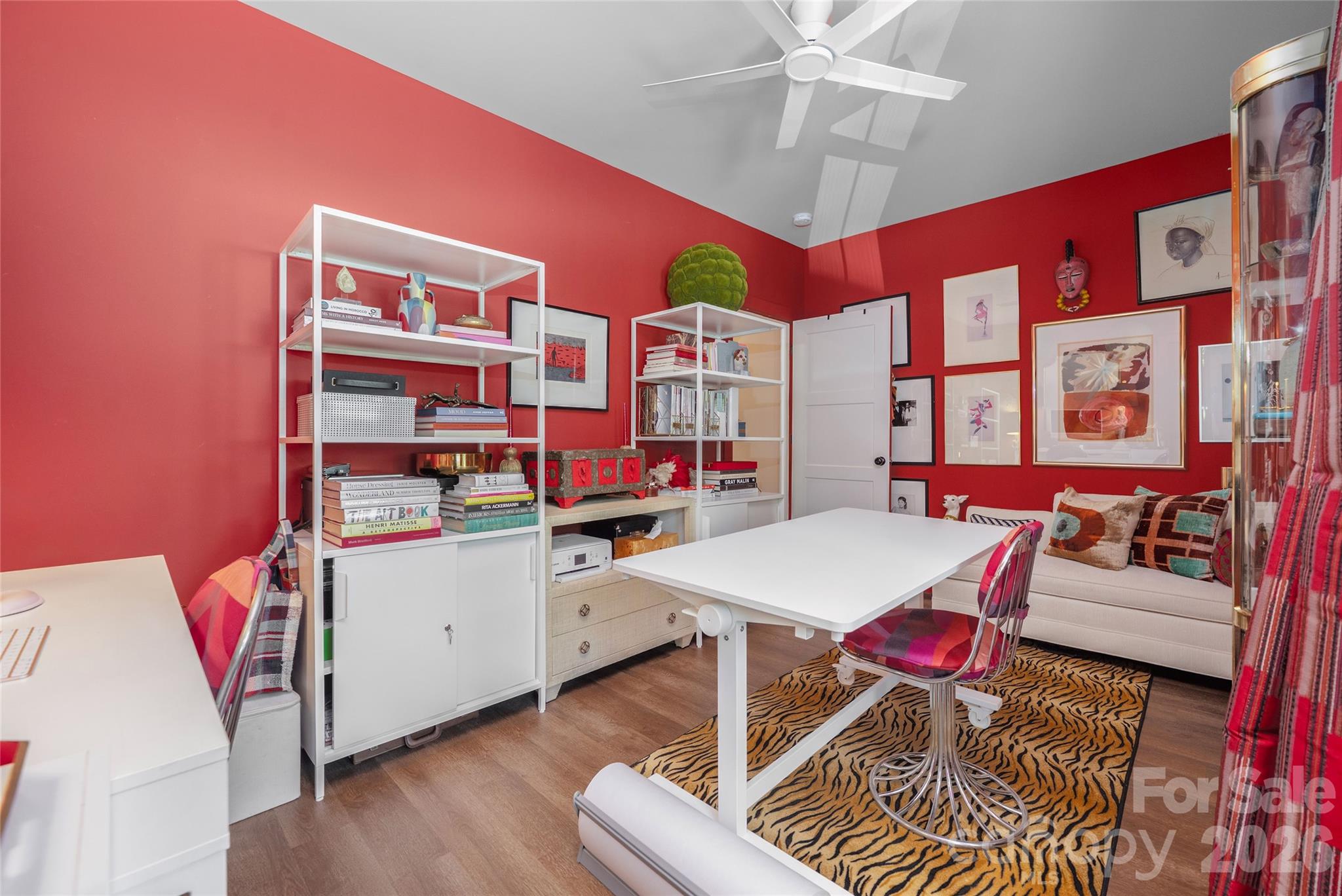 Home office with vivid red walls, white shelving, a sofa, and a tiger-stripe rug.