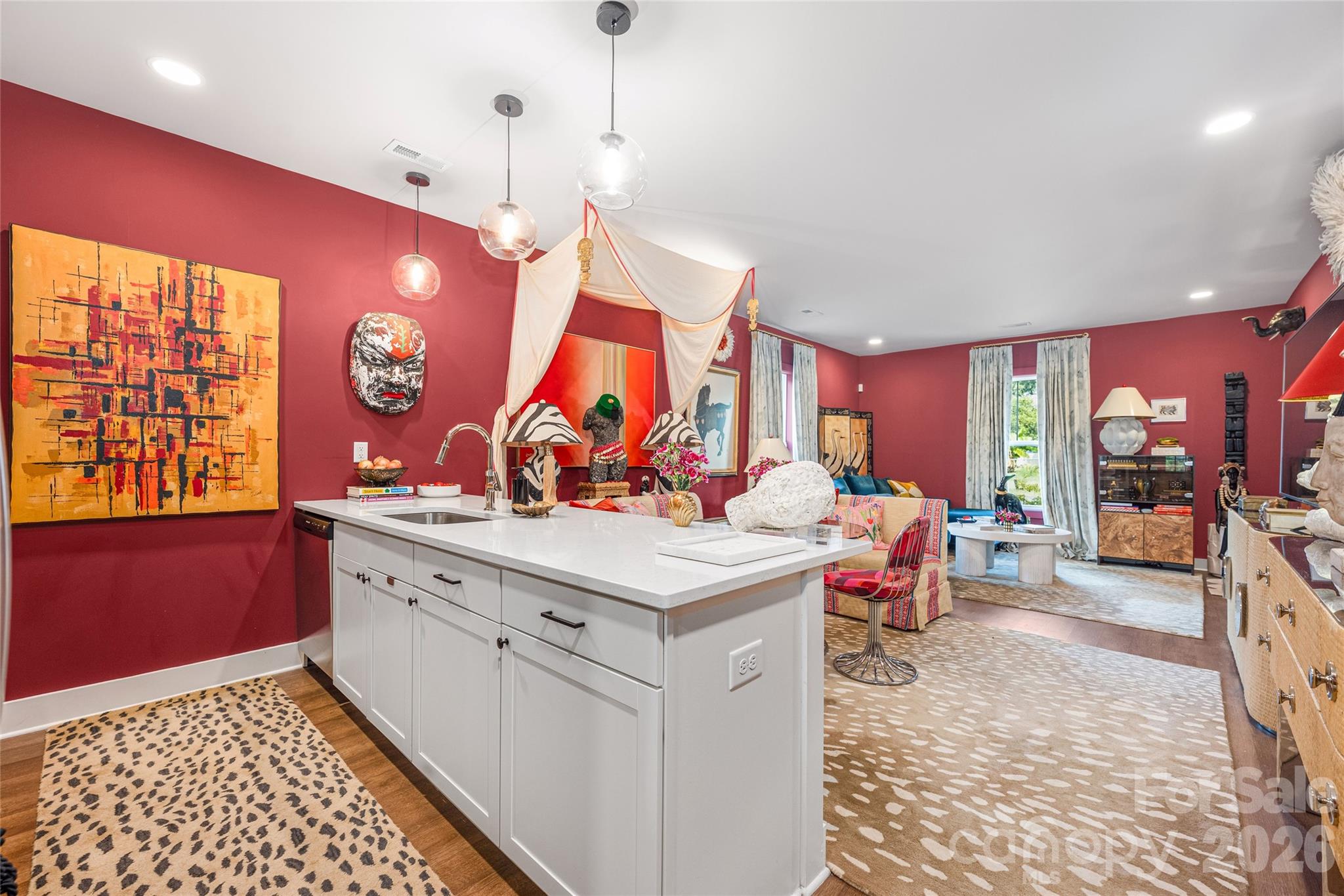 Kitchen and living area with a large white island, red walls, and colorful artwork.