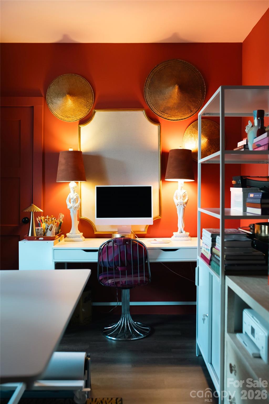 Furnished home office with red-orange walls, a white desk, shelving, and woven wall baskets.