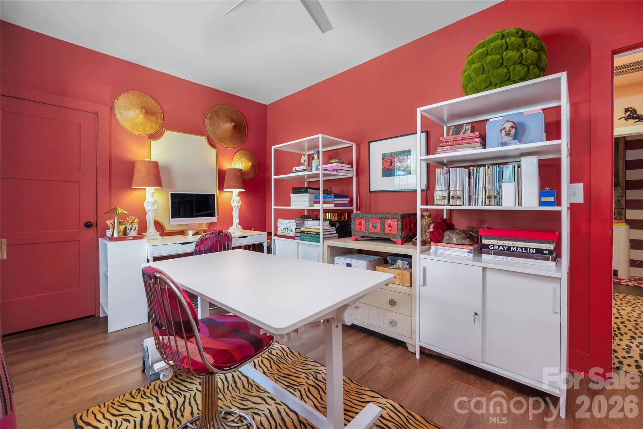 Home office with vivid red walls, white desk and shelving, and a tiger-stripe rug.
