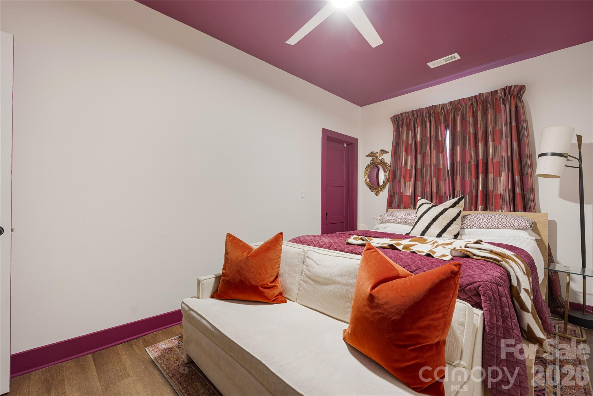 Bedroom with a plum ceiling and quilt, patterned curtains, and a cream sofa with orange pillows.