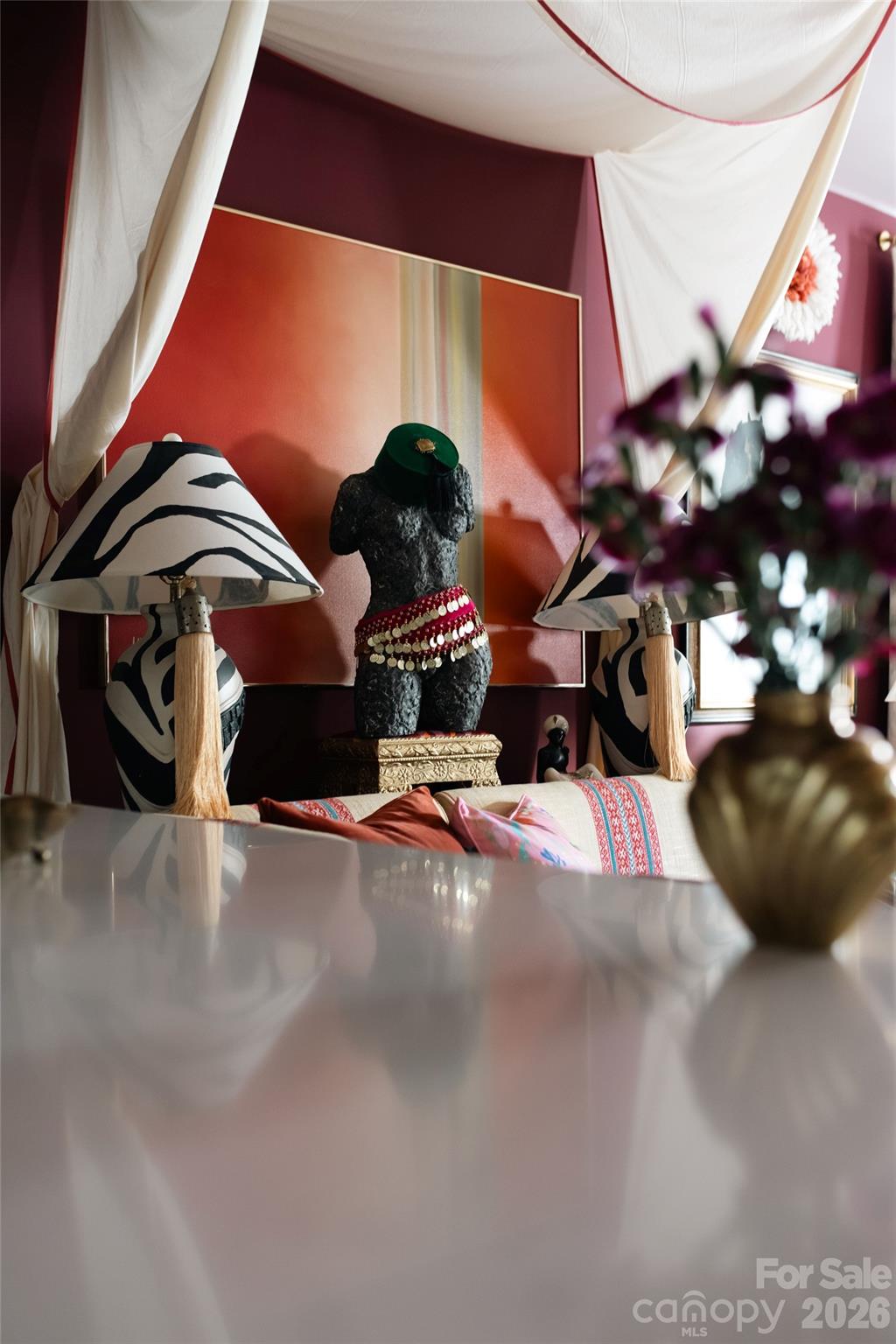 Colorful sitting area with a draped white canopy, patterned lamps, and a sculptural figure.