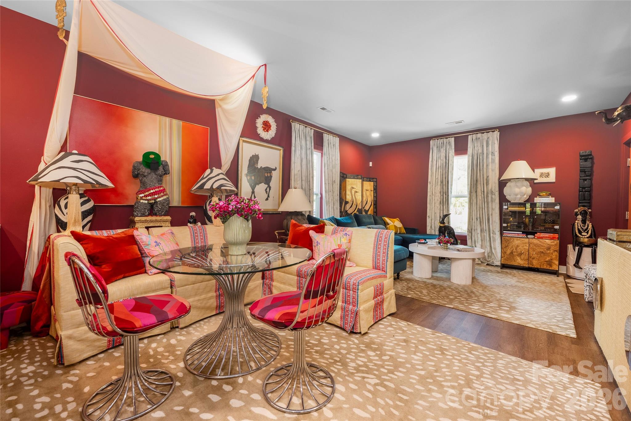 Living room with deep red walls, cream sofas, colorful cushions, and a glass dining table.