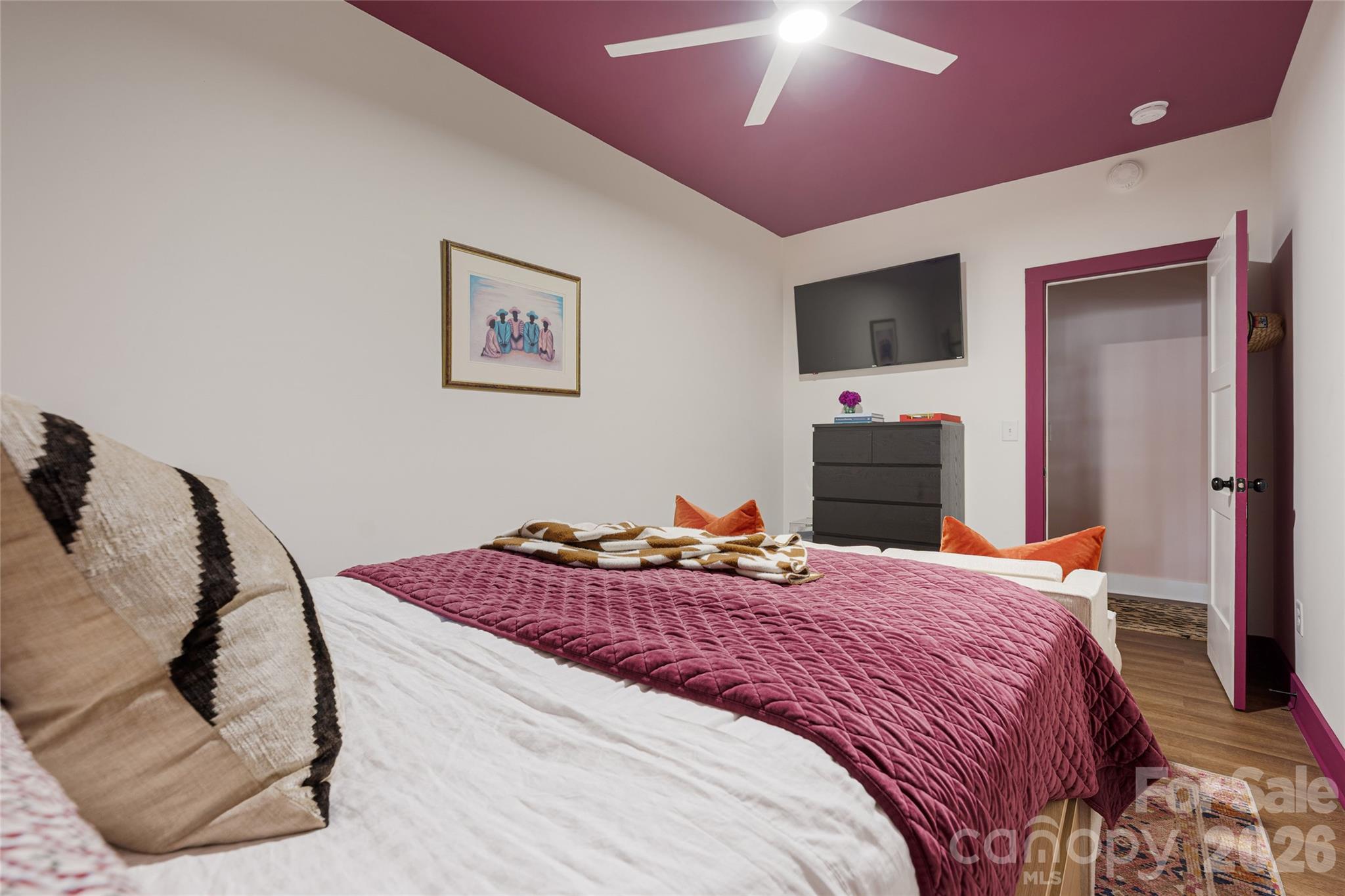 Furnished bedroom with a plum quilt, bold plum ceiling, and wall-mounted television.