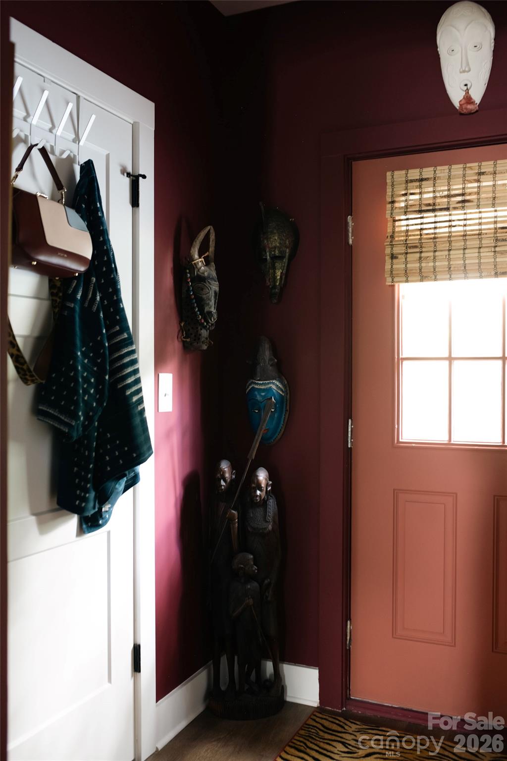 Entryway with a coral front door, burgundy walls, coat hooks, and carved decorative figures.