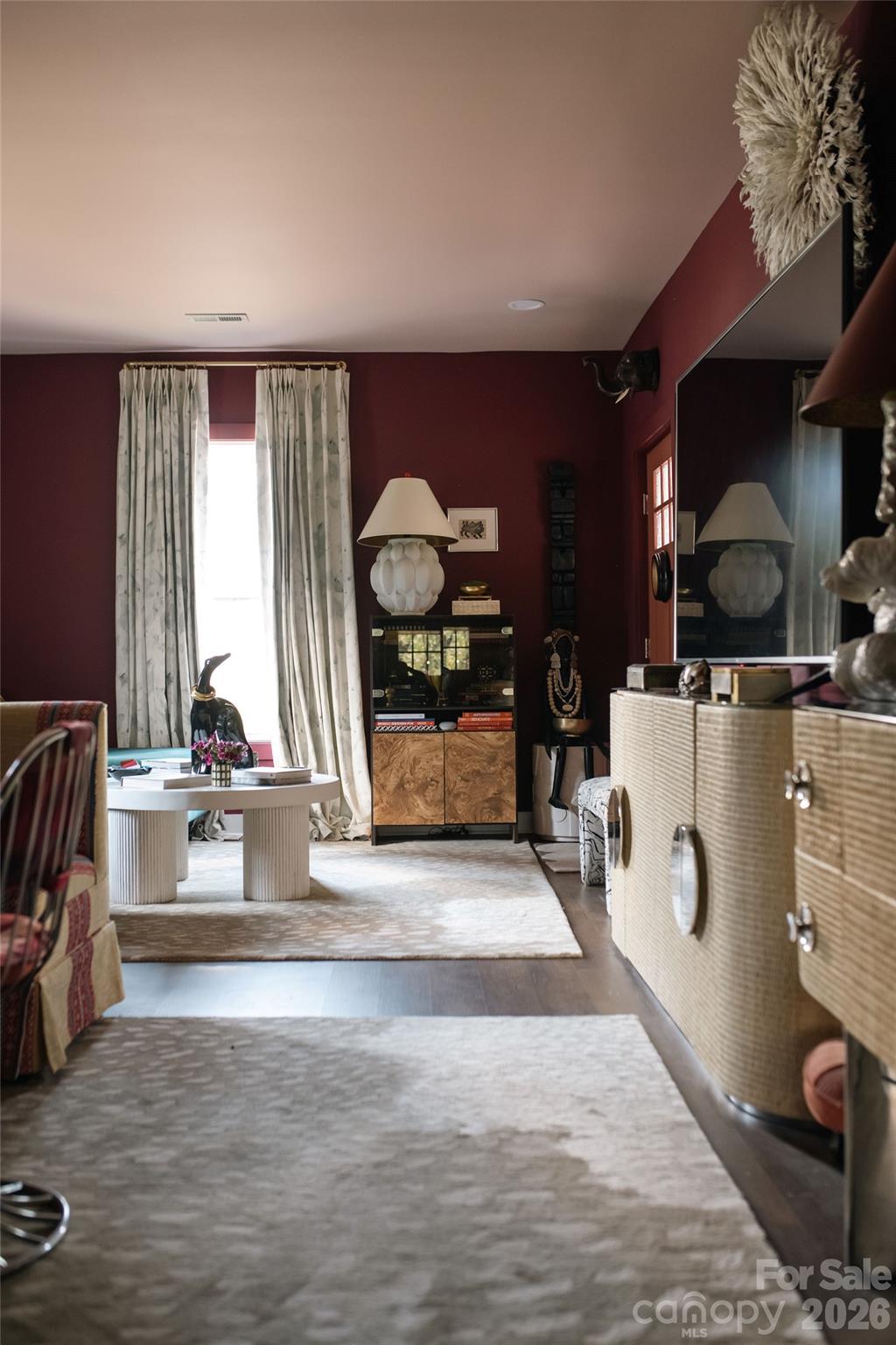 Living room with deep red walls, a bright curtained window, and a round white coffee table.