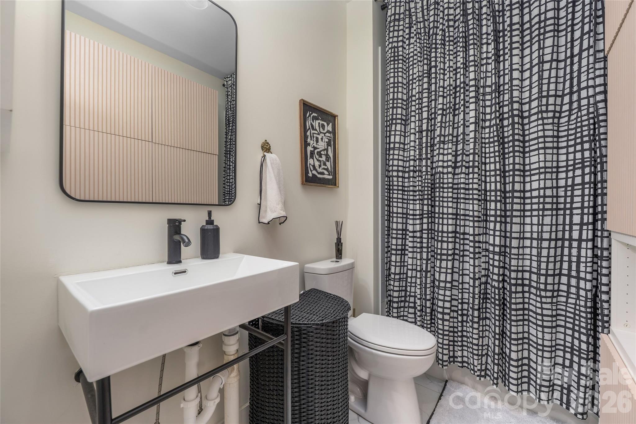 Bathroom with a sculptural white sink, black woven hamper, and geometric black-and-white shower curtain.