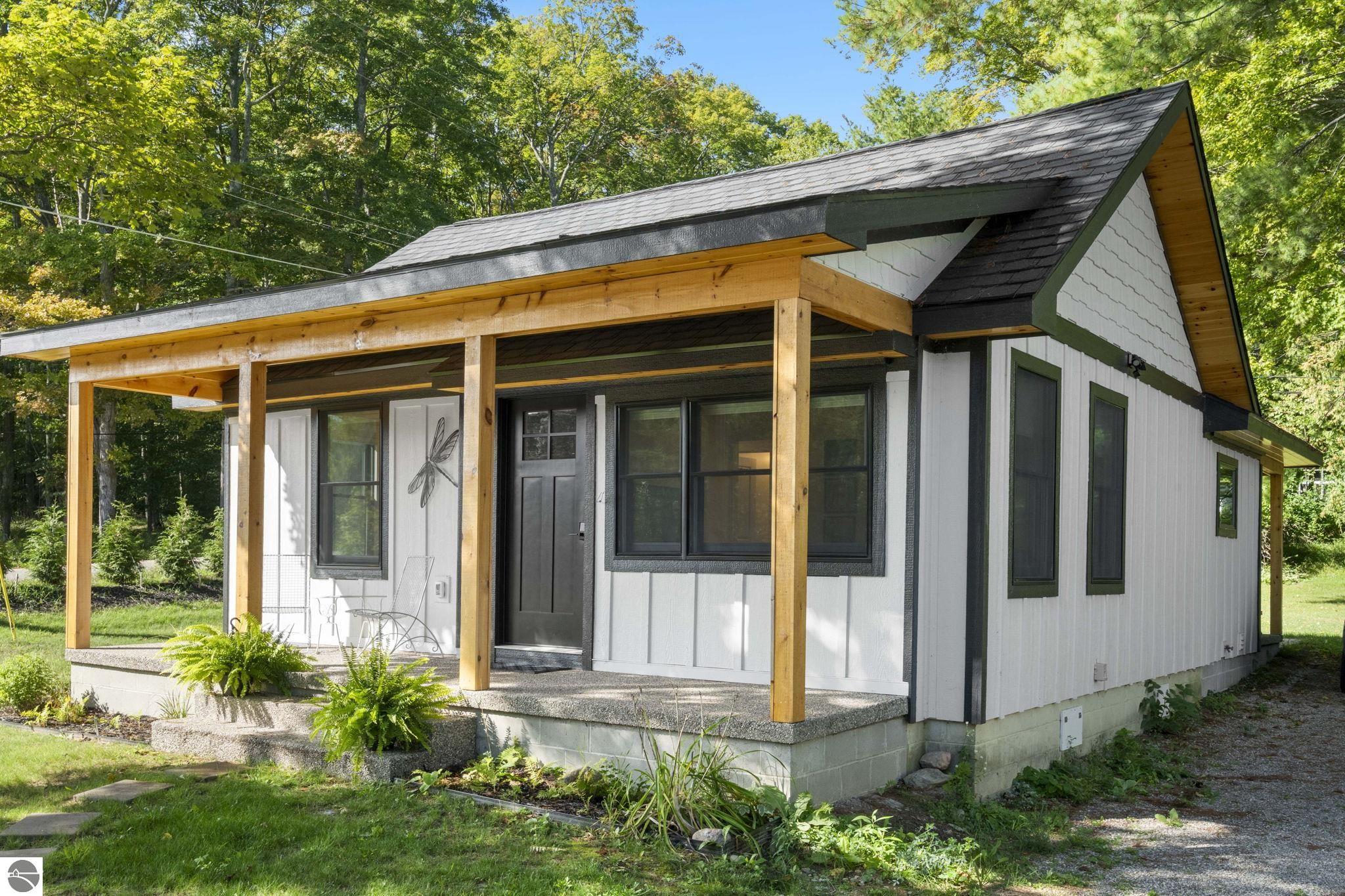Modern white cabin with a timber-post porch nestled among trees.