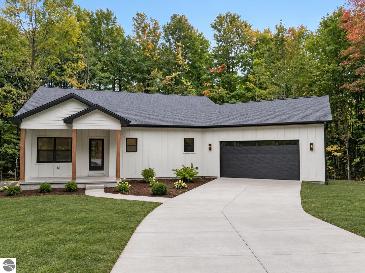 White single-story home with covered porch, attached garage, and wide driveway amid autumn trees.