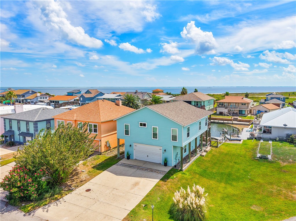 Light blue two-story coastal home beside a canal, with the bay visible in the distance.