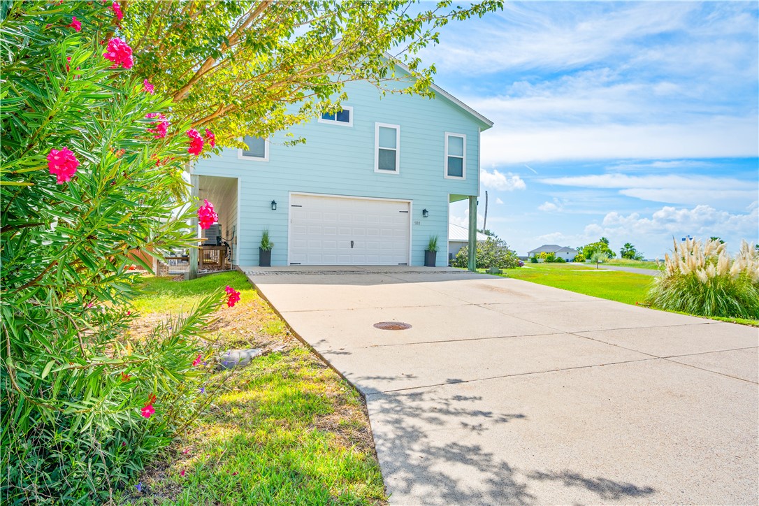 Light blue two-story house with a double garage, wide driveway, and pink flowering shrubs.