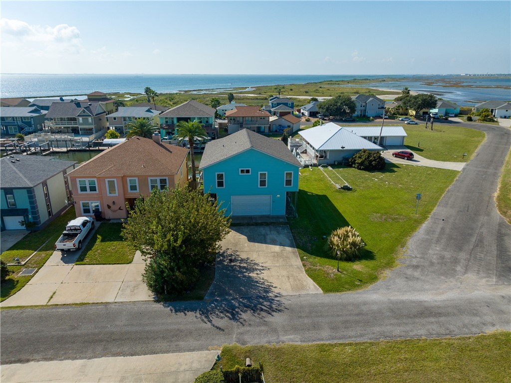 Turquoise two-story coastal home with a garage, neighboring houses, marshland, and open water.