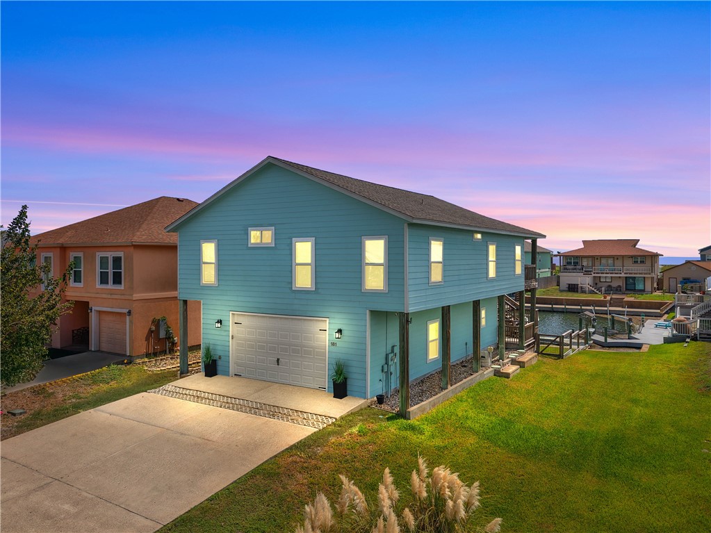 Blue two-story coastal home with a garage beside a canal at dusk.