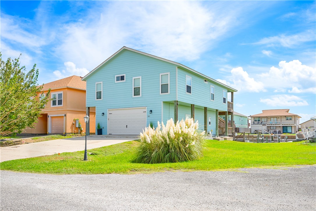 Pale aqua two-story coastal home with a garage, raised living area, and canal-side docks.