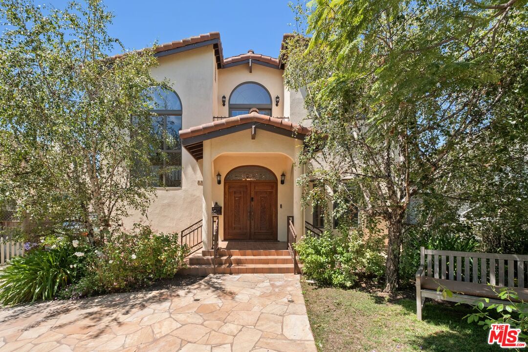 Two-story stucco home with arched windows, wooden double doors, and a stone garden walkway.