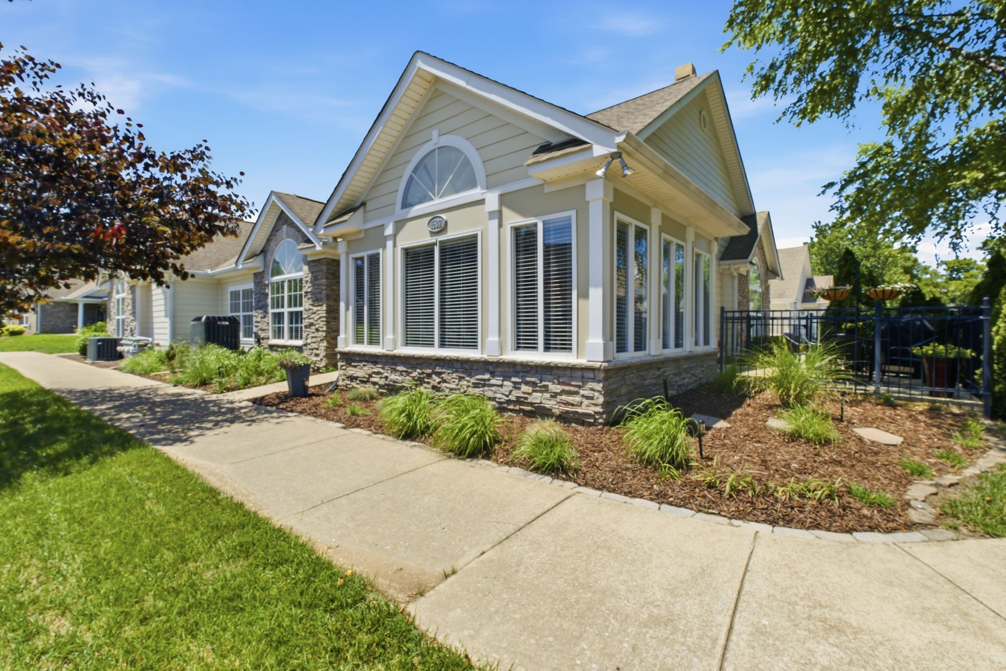 Condominium exterior with arched windows, stone accents, landscaped beds, and a fenced patio.