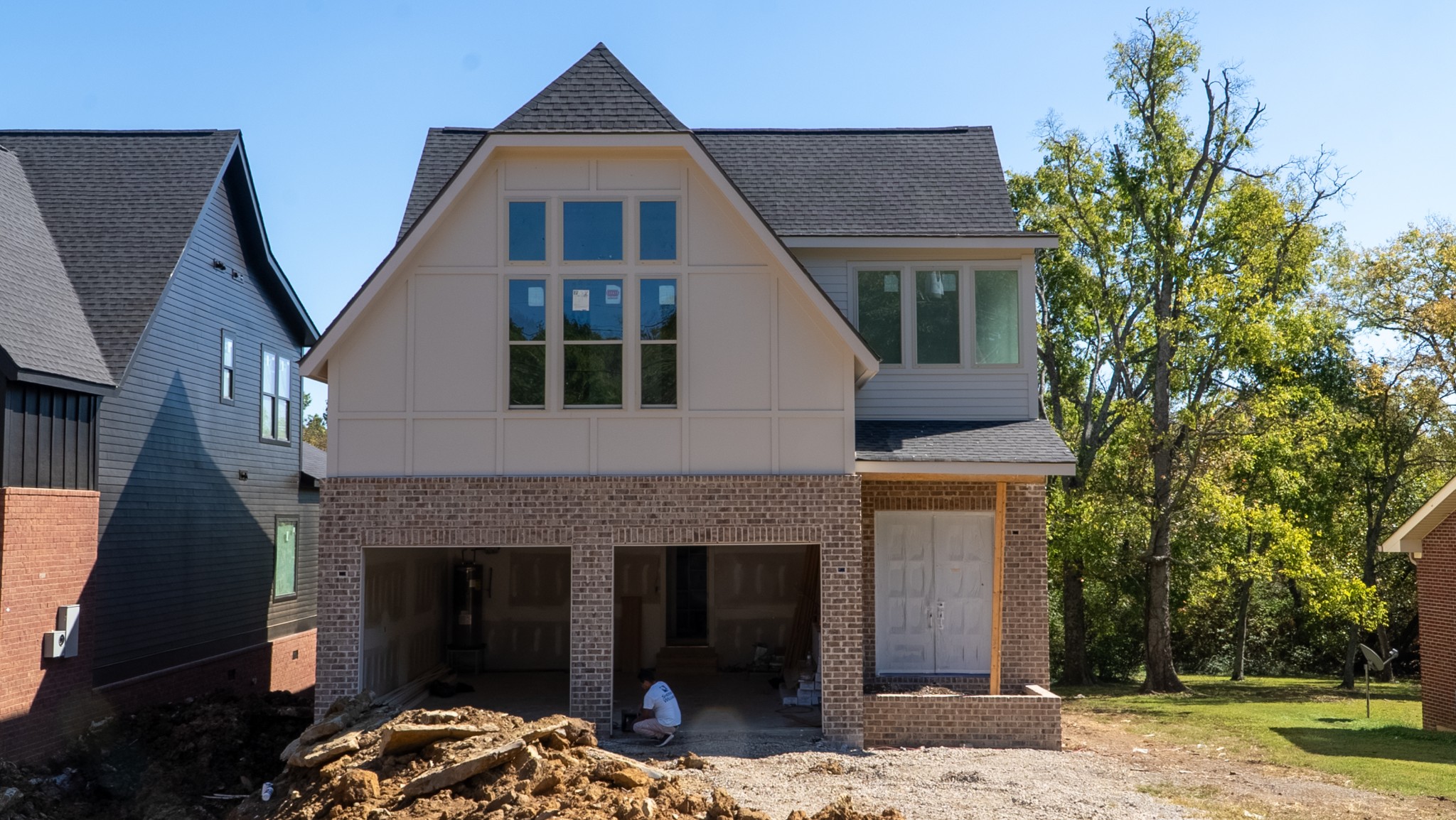 House under construction with a steep central gable, brick lower facade, and unfinished garage.