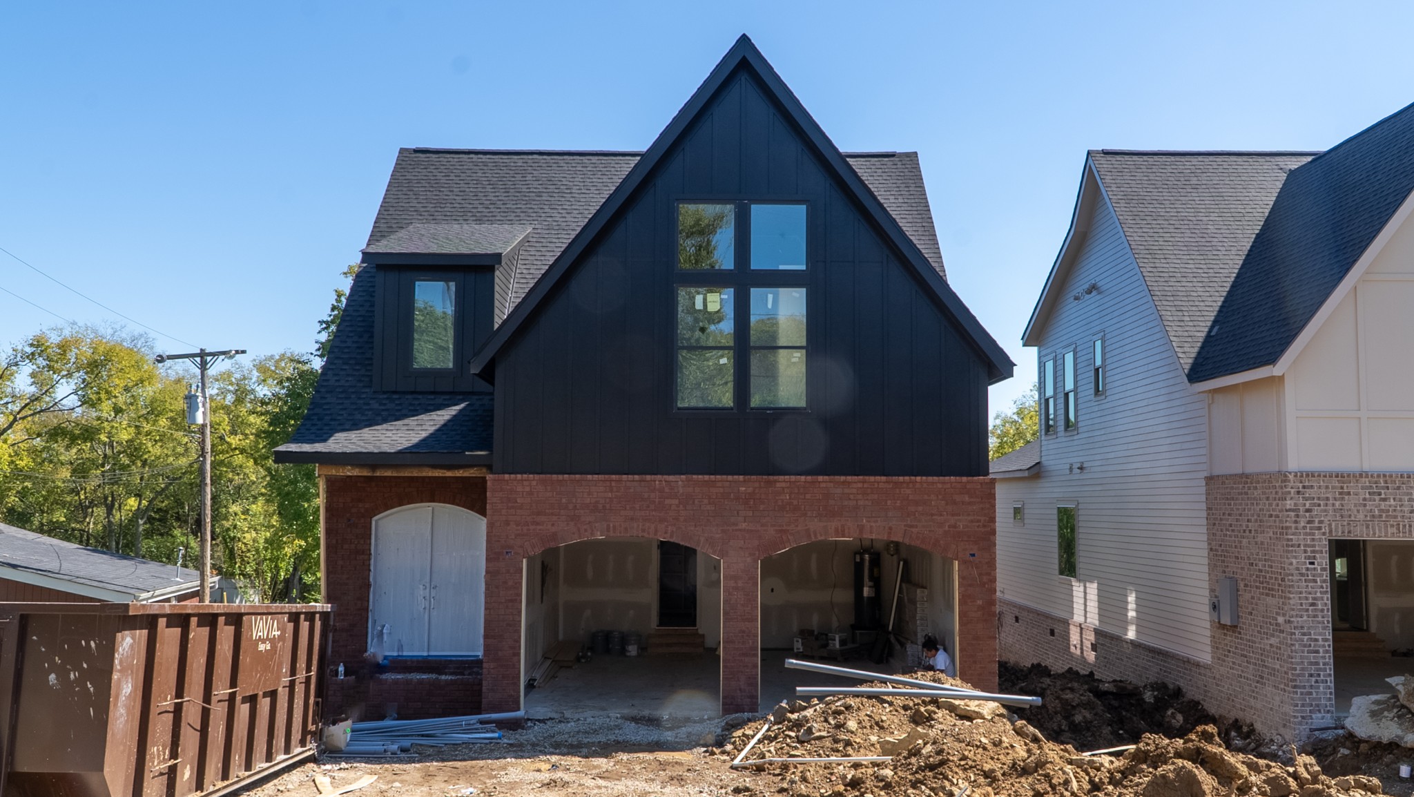 House under construction with a black gabled facade, brick lower level, and arched garage openings.