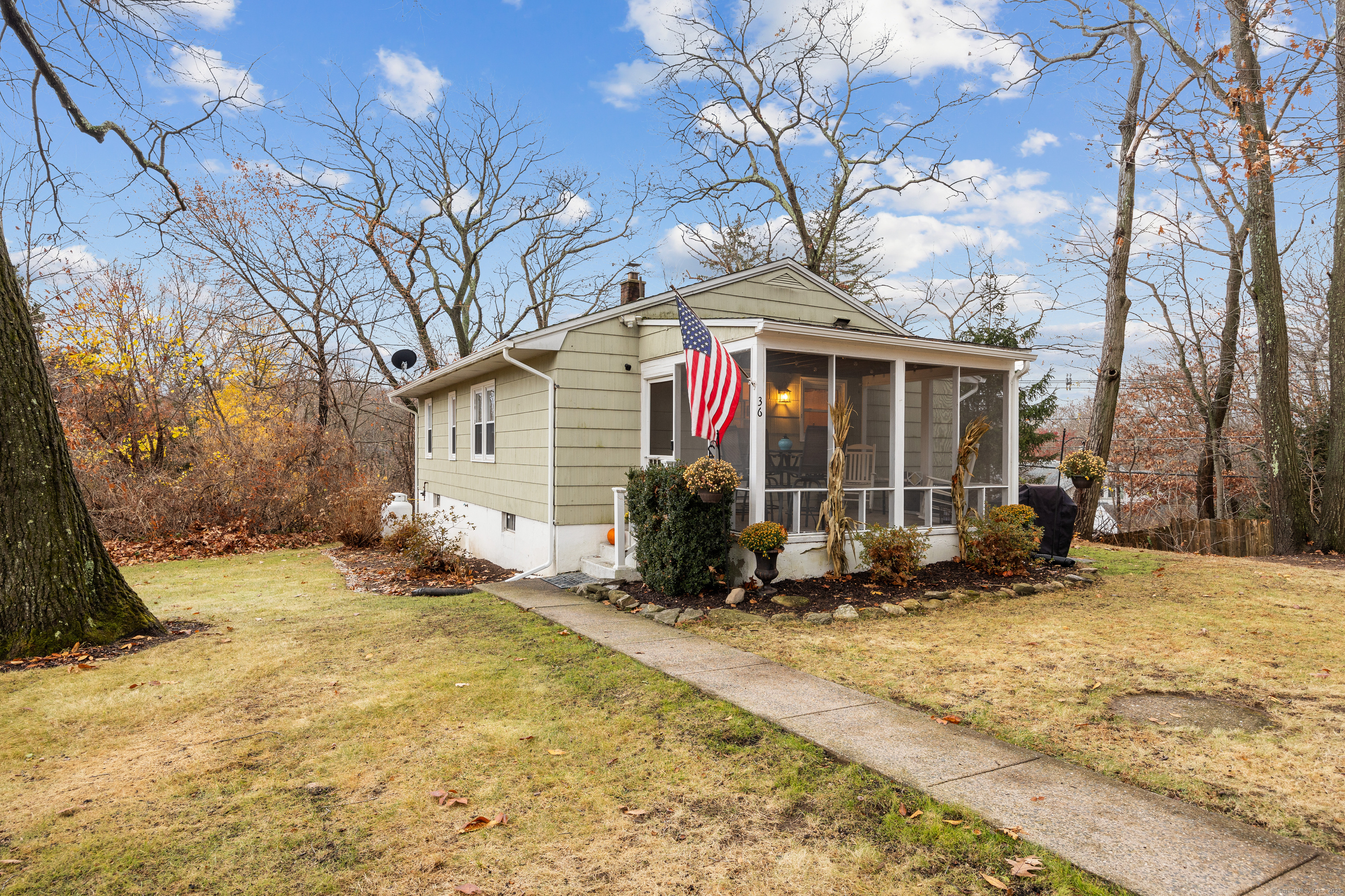 Single-story home with a screened porch, American flag, and walkway through an autumn lawn.