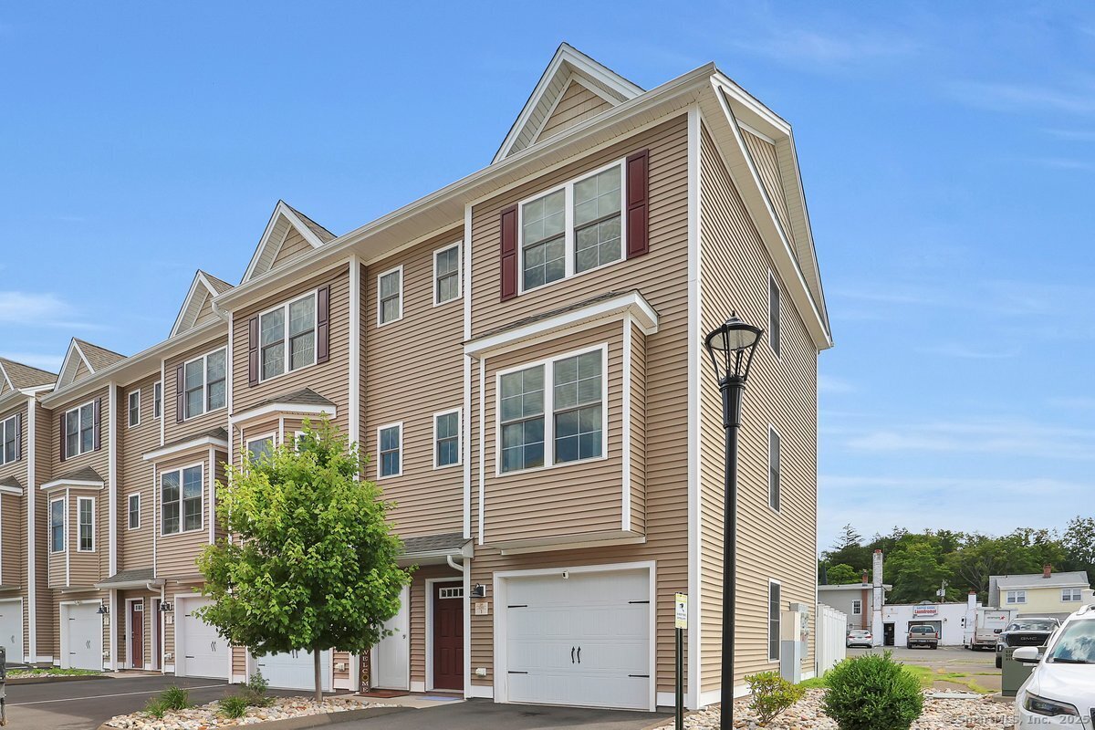 Tan multi-story townhome with white-trimmed windows, red shutters, and an attached garage.