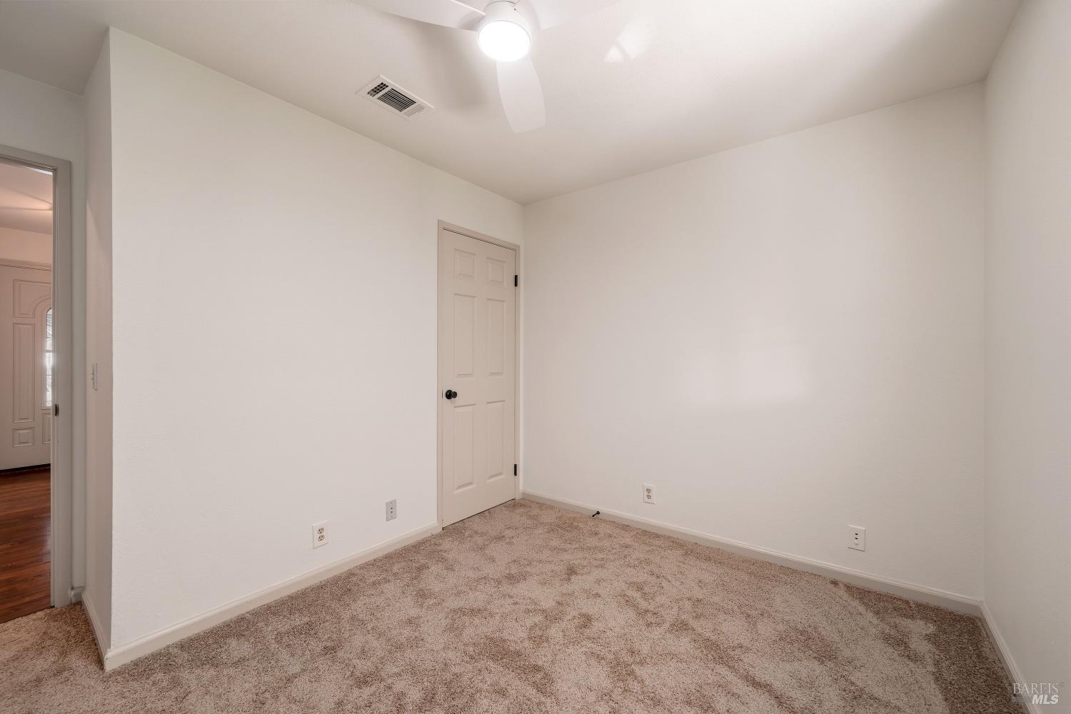 Empty bedroom with beige carpet, a paneled closet door, and a ceiling fan with light.