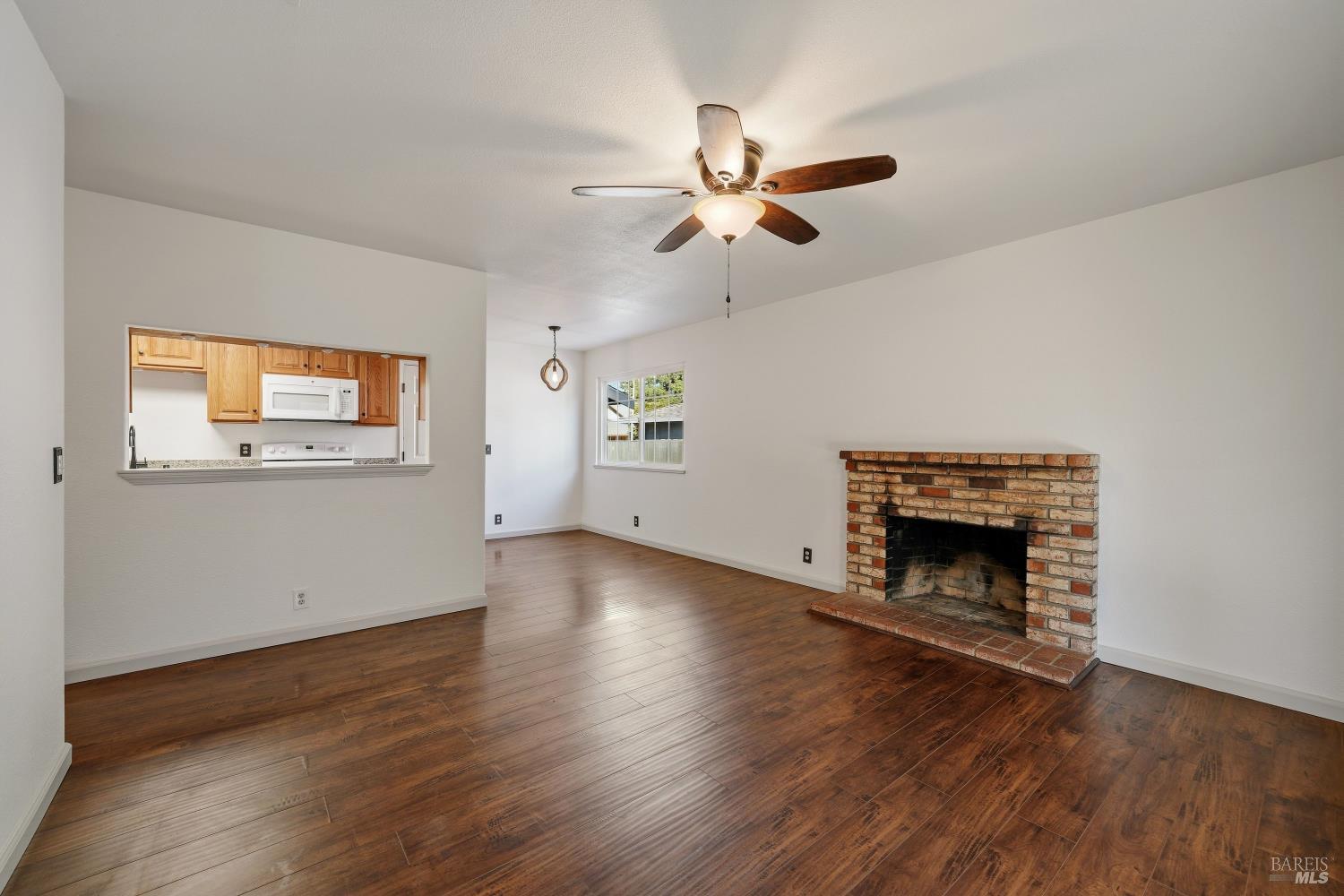 Living room with dark wood floors, a brick fireplace, and a pass-through opening to the kitchen.