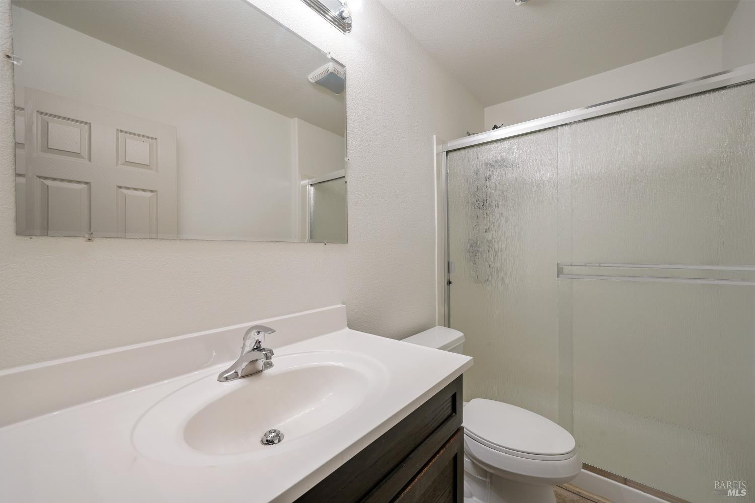 Bathroom with a white sink, dark vanity, toilet, and frosted sliding shower doors.