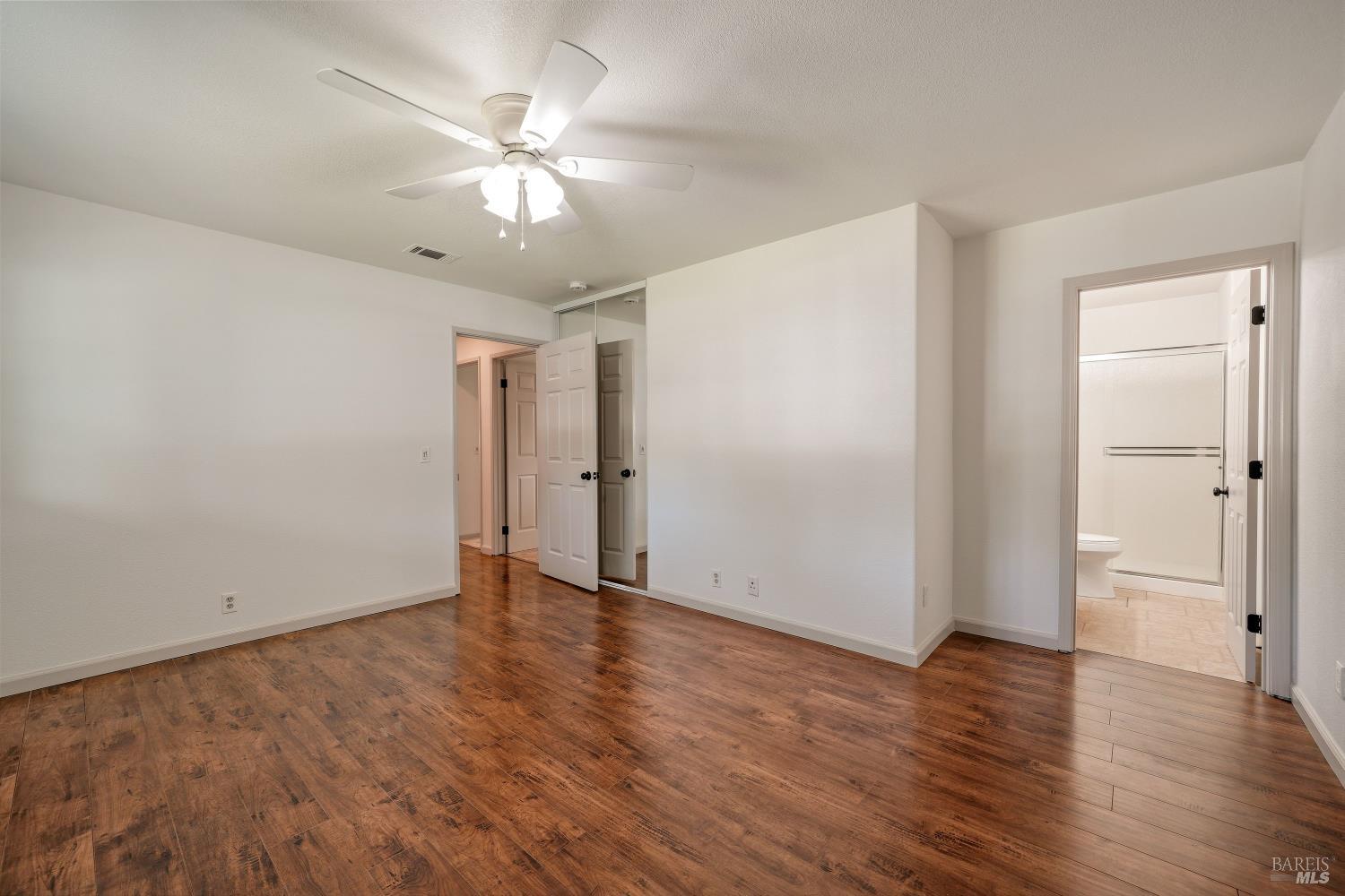Vacant bedroom with dark wood floors, mirrored closet doors, and an attached bathroom.