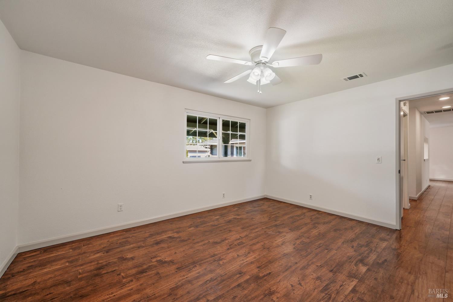 Empty room with wood-look flooring, a ceiling fan, and a window overlooking a covered area.