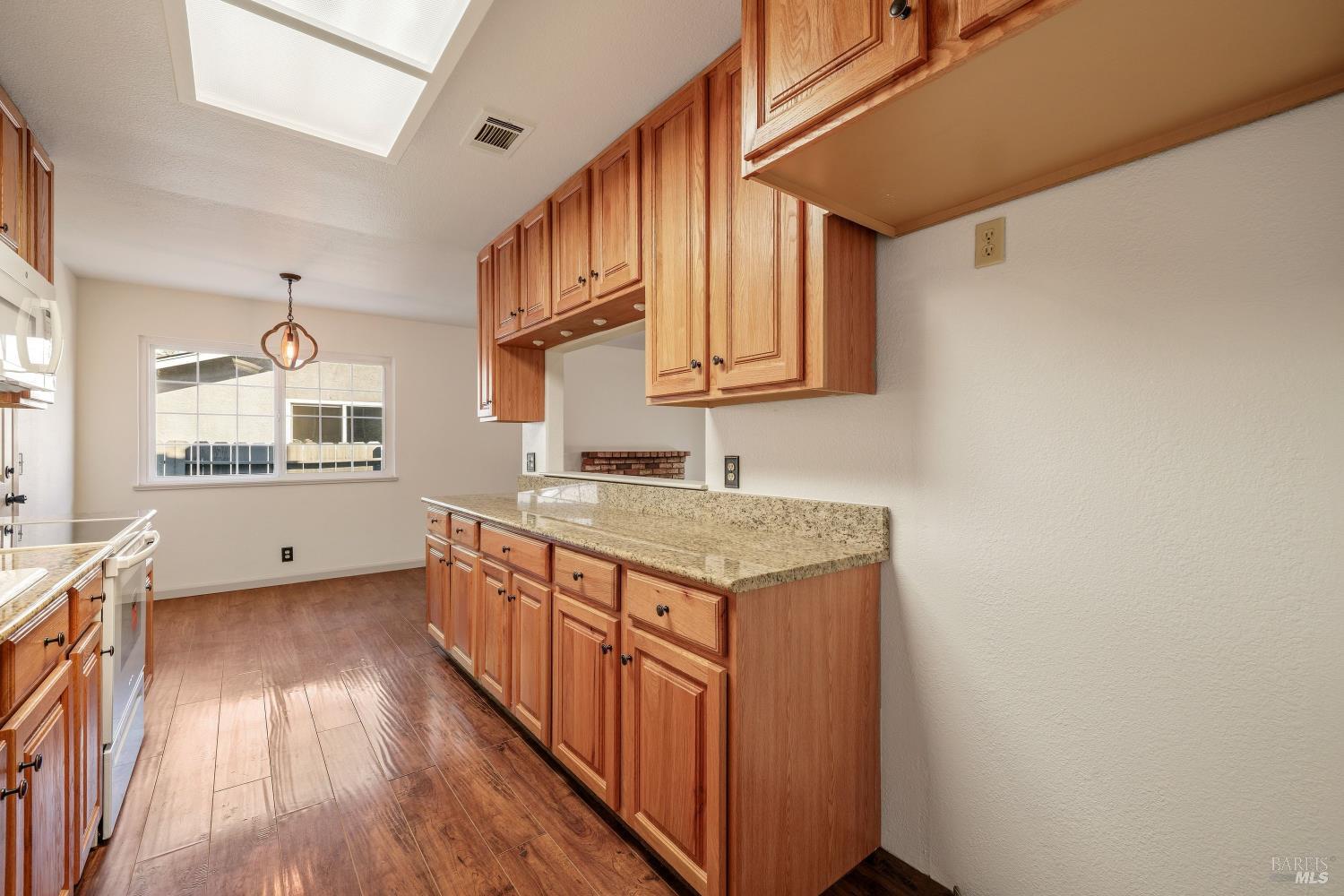 Kitchen with warm wood cabinets, granite countertops, and a large skylight.